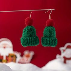 two knitted green and red christmas hats hanging from a clothes line with snow on the ground