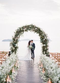 a bride and groom are standing under an arch with flowers on it, surrounded by candles