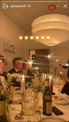 people sitting at a table with wine bottles and candles in front of them, while one person is taking a selfie