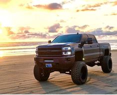 a large truck parked on top of a sandy beach next to the ocean at sunset