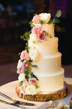 a three tiered wedding cake with pink and white flowers on the top is sitting on a table