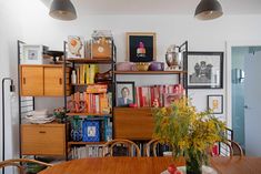 a wooden table topped with lots of books next to a shelf filled with pictures and vases