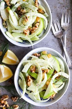 two bowls filled with food next to silverware and lemon wedges on a table