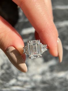 a woman's hand holding an engagement ring with two baguettes on it