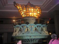 a light fixture in the middle of a room with people standing around and looking at it