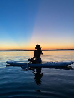 a woman sitting on top of a surfboard in the middle of water at sunset