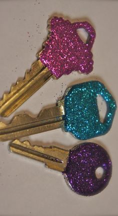 three gold and purple glittered keys are on a white surface, with one key missing