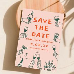 a pink save the date card sitting on top of a wooden plate with wine glasses