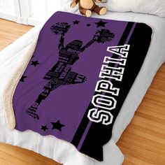 a bed with a purple and black blanket on top of it next to a teddy bear