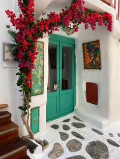 a green door with red flowers growing over it and stone steps leading up to the entrance