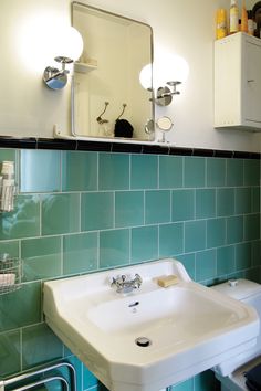 a bathroom with green tiled walls and blue flooring is pictured in this image, there are two mirrors on the wall above the sink