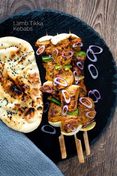 some food is on a black plate with skewered onions and other foods around it