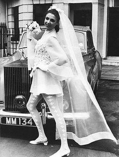 a woman standing next to a car in front of a building with a veil on her head