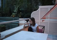 a woman sitting at an outdoor table drinking from a cup while looking out the window