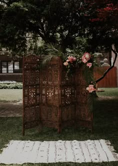 a wooden screen sitting on top of a grass covered field next to a flower filled tree