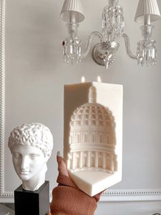 a person is holding up a sculpture in front of a white wall and chandelier