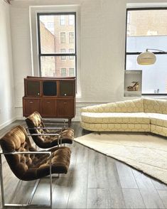 a living room filled with furniture next to windows and a rug on top of a hard wood floor