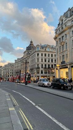 a city street with cars parked on both sides and buildings in the background at sunset