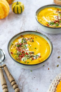 two bowls filled with soup and garnished with chopped vegetables on the table next to pumpkins