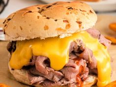 a close up of a sandwich with meat and cheese on the bun, surrounded by sweet potato chips