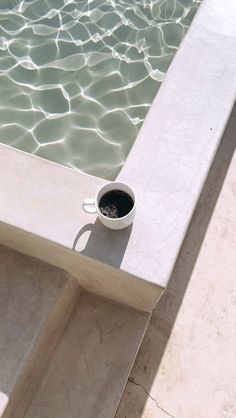 a cup of coffee sitting on top of a table next to the water's edge