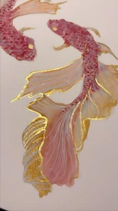 two gold fish with pink tails are on a white surface