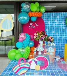 a table topped with balloons and cake next to a blue tiled wall in front of a window