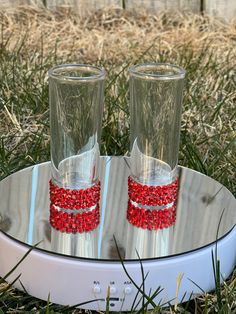 two wine glasses with red beads on them sitting in the grass next to each other