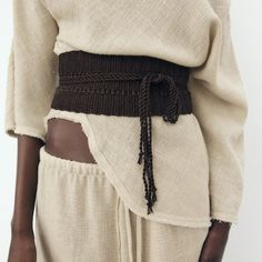 a close up of a person wearing a white shirt and brown belted skirt with black accents