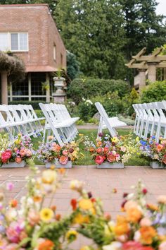 rows of white folding chairs with colorful flowers on the ground in front of a house