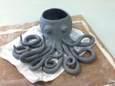 an octopus sculpture sitting on top of a piece of paper next to a cup and scissors