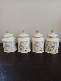 four ceramic canisters sitting on top of a wooden table next to a wall