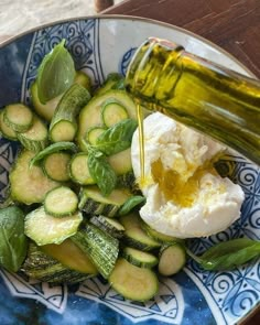 a blue and white plate topped with cucumbers and an olive oil being drizzled on top