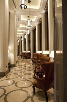 an elegant hallway with chairs and lamps on either side of the corridor, leading to another room