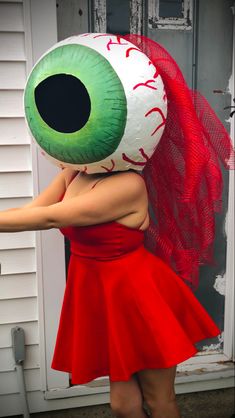 a woman in a red dress with an eyeball on her head and hands behind her back