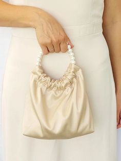 a woman in a white dress holding a beige purse with pearls on it's handle