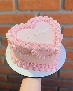 a pink heart shaped cake sitting on top of a white plate next to a brick wall