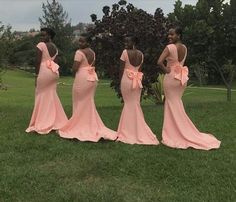 four women in pink dresses standing on grass with their backs turned to the camera and looking at each other