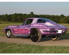 a purple car parked on the side of a road next to a lush green field