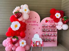 there is a pink and red birthday party set up with balloons, strawberries, and flowers