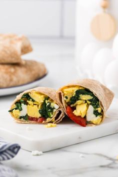 an egg, spinach and tomato wrap on a cutting board next to some pita bread