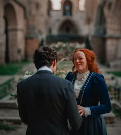 a man and woman standing next to each other in front of an old stone building