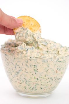 a hand dipping a cracker into a bowl of dip