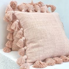 a pillow with tassels on it sitting next to a white wall and cement block