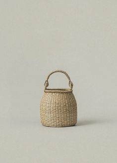 a small woven basket with handle on the front and side, against a gray background