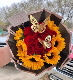 a bouquet of sunflowers, roses and butterflies is held by someone's hand