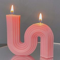 two lit candles sitting next to each other on top of a glass table in front of a gray wall