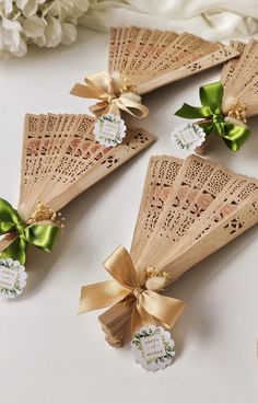 four wooden fan shaped favors with ribbons and tags attached to them, sitting on a table