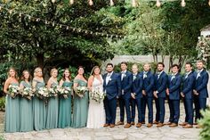 a group of people standing next to each other in front of trees and bushes at a wedding