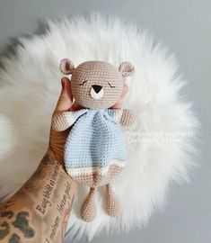 a hand holding a crocheted teddy bear with a blue dress on it's chest